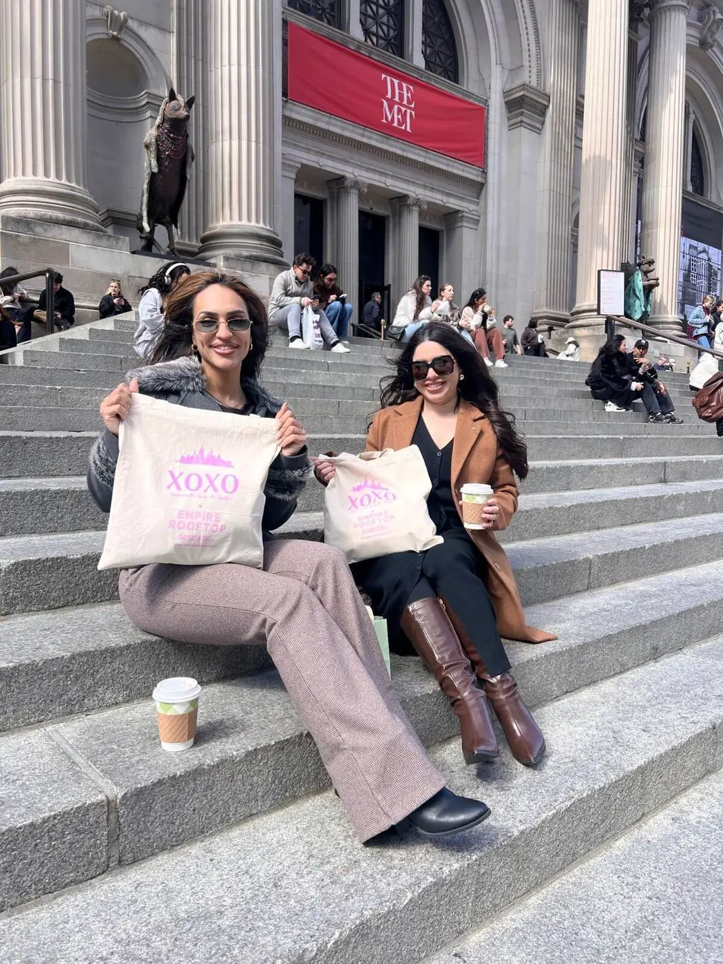 Zwei Gäste mit XOXO-Stofftaschen und Kaffee auf den Met Steps